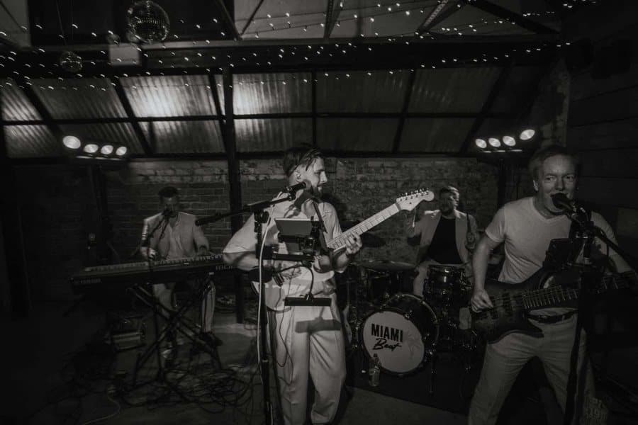 Black and white shot of Miami Beat playing under festoon lights and a glitter ball at The Shack Revolution