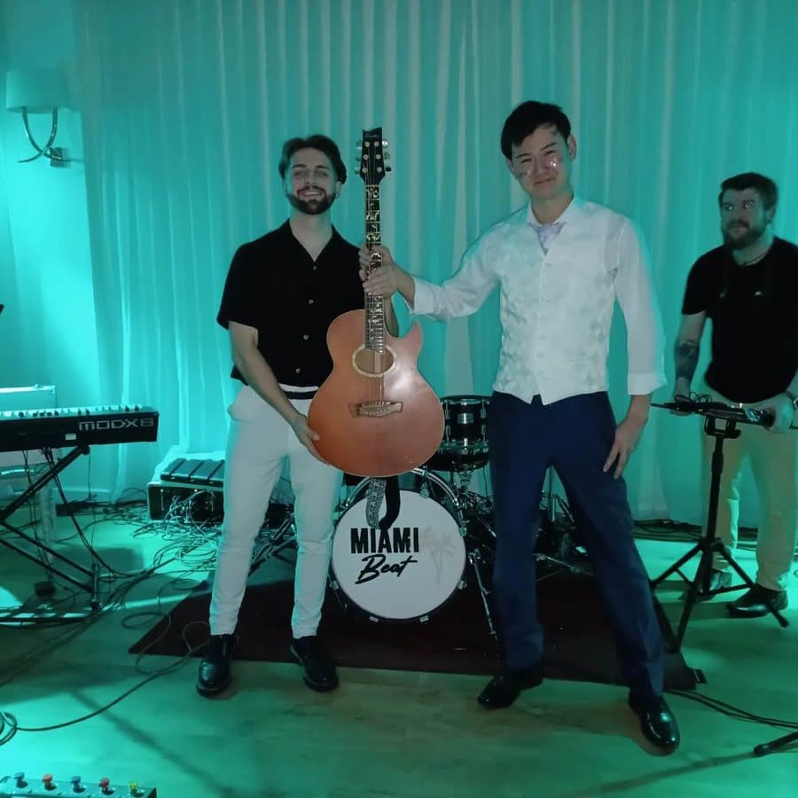 Two guests holding an acoustic guitar in front of the band's drum kit, lit green